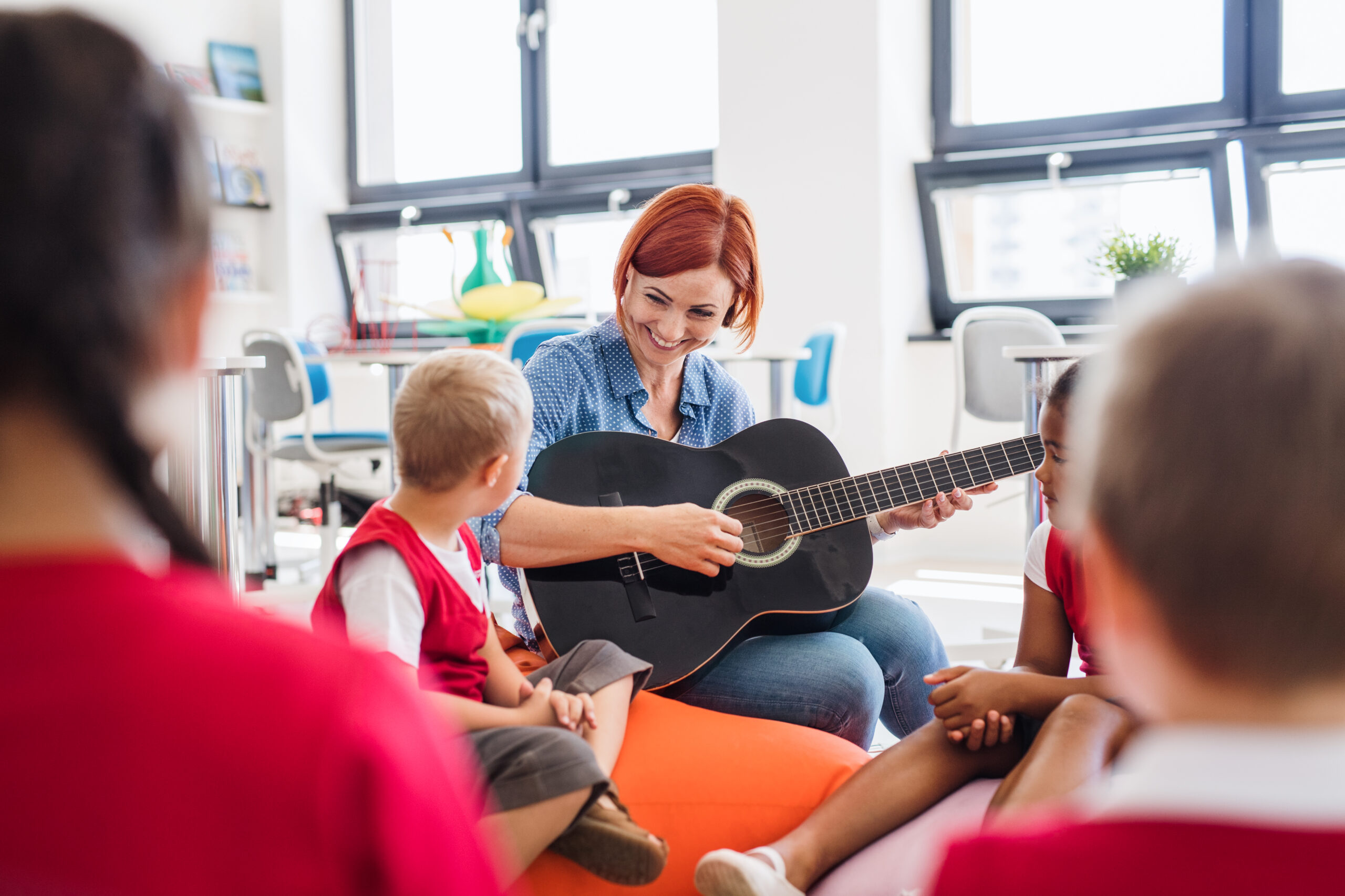 A group of small school kids and teacher with guitar sitting on the floor in class. A group of small school kids and teacher with guitar sitting on the floor in class, singing.