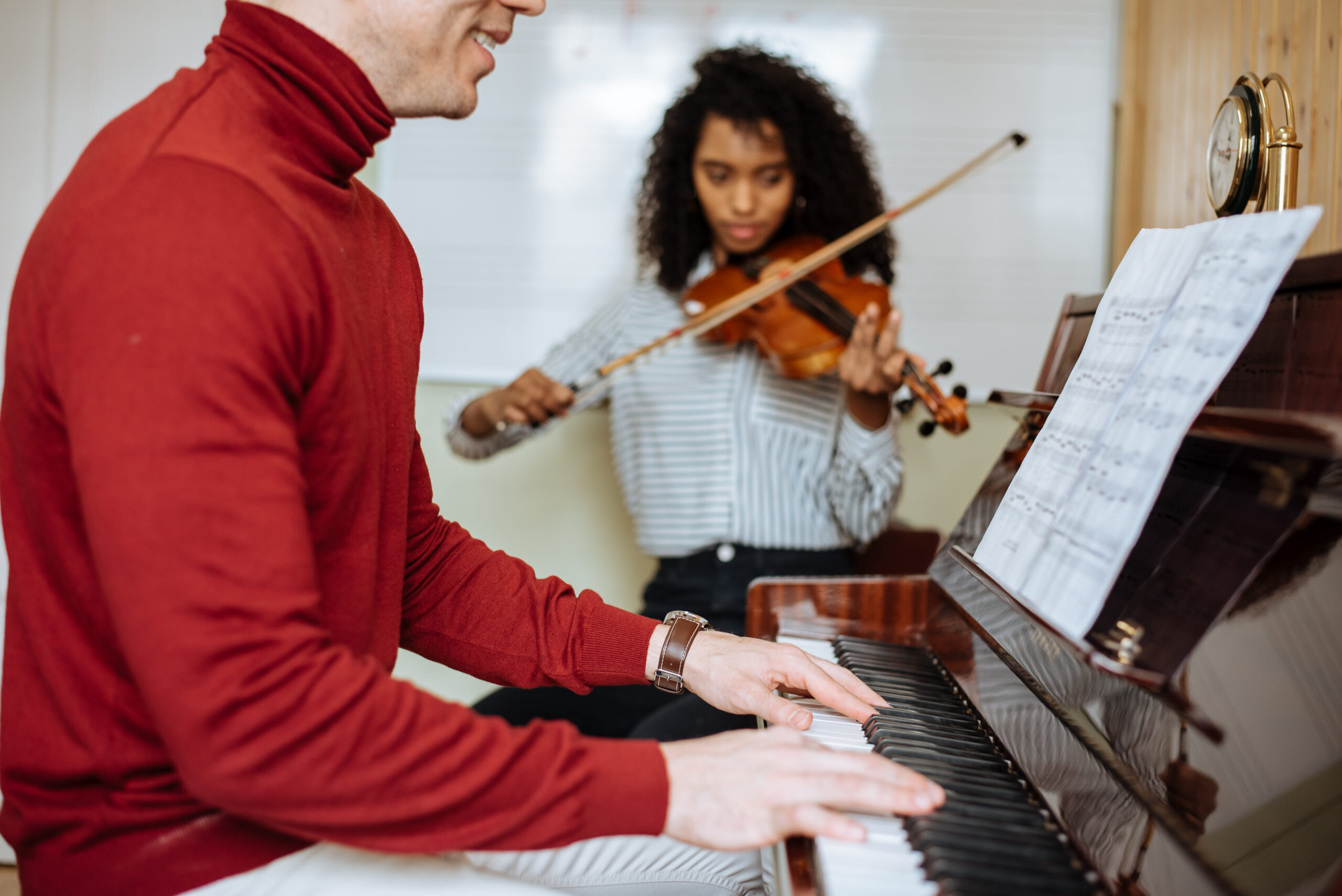Man playing piano near woman playing violin in studio Side view of young man playing piano near black woman playing violin in music studio